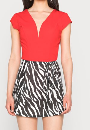 Haut rouge à col en V avec des manches courtes associé à une jupe à imprimé zèbre noir et blanc, dotée d'un lien à la taille et d'une texture de tissu lisse.