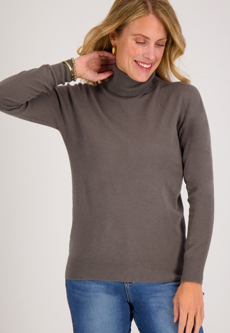 Grijze coltrui met een zachte textuur, met lange mouwen en een geribbelde zoom. Gecombineerd met blauwe jeans, tegen een effen achtergrond.