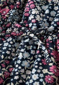 Tejido estampado floral en azul marino, con pequeñas flores en tonos rosa, blanco y azul claro. El material es suave, con una cinturilla elástica y un detalle de lazo anudado.