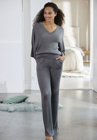Grijze geribbelde gebreide trui met een V-hals en bijpassende wijde broek, voorzien van voorzakken en een relaxte pasvorm. Zachte textuur, casual ontwerp.