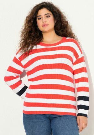 Maglione a righe rosse e bianche con collo a giro e maniche lunghe, una manica presenta dettagli in blu navy. Indossato con jeans blu.
