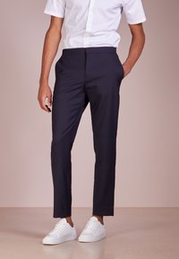 Námořnické modré kalhoty na míru s elastickým pasem, hladkým povrchem a slim fit, doplněné o bílé tenisky a krátký rukáv bílou košili.