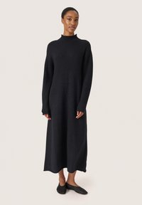 Rochie lungă neagră cu guler înalt, realizată dintr-un material moale, având mâneci lejere și o siluetă fluidă care ajunge până la glezne.