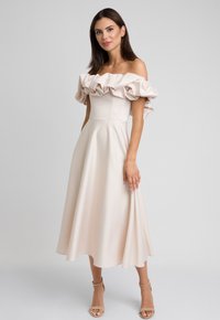 Sukienka odsłaniająca ramiona w jasnym beżu z falbaniastymi rękawami, dopasowanym korpusem i luźną spódnicą w kształcie litery A, wykonana z gładkiego materiału.