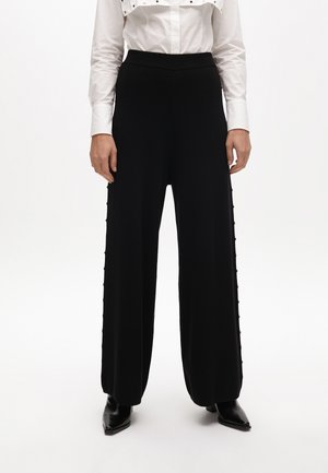 Black wide-leg pants with a high elastic waistband and button details along the side seams, made from soft, textured fabric.