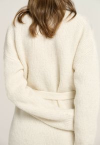 Cremfarbener gestrickter Cardigan mit strukturiertem Muster, übergroßen Ärmeln und einem Taillenzug. Weiches, gemütliches Material, von hinten gezeigt.