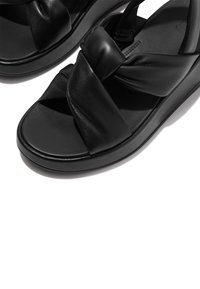 Svarta lädersandaler med tvinnad ovandel, platt sula och en slät yta, med en sömlös och minimalistisk stil.