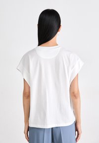 T-shirt bianco in cotone con maniche corte, scollatura rotonda e orlo curvo. Il tessuto risulta liscio e leggero.