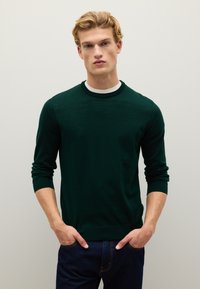 Maglione verde scuro a collo rotondo e maniche lunghe, realizzato in tessuto leggero, abbinato a jeans blu scuro.