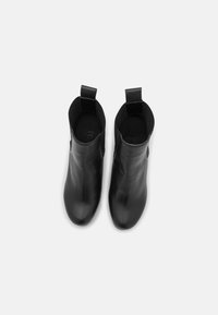 Czarne skórzane botki za kostkę o gładkiej fakturze, zaokrąglonym nosku i minimalistycznym wzornictwie. Posiadają pętle do zakładania oraz subtelne logo z boku.