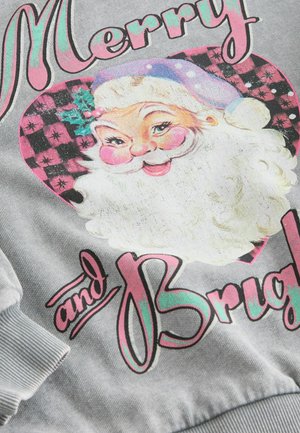 Joulupukki punaposkinen ja violetti hattu pinkki-mustapartaisella sydämellä, jossa on teksti "Iloista ja Kirkkaita" harmaalla kankaalla.