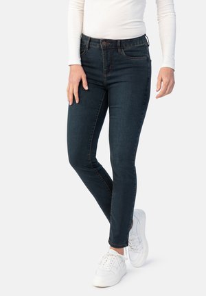 Dunkelblaue Skinny Jeans mit mittelhohem Bund, Vorderaschen und Knopfverschluss, kombiniert mit weißen Sneakers.