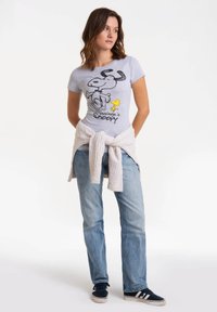 Gray cotton t-shirt featuring Snoopy and Woodstock graphic with "Happiness is Snoopy" text. Paired with light blue jeans and a light sweater tied at the waist.