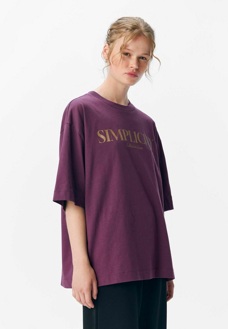 Losse fit, korte mouwen t-shirt in diep paars katoen. Bevat gouden tekst "SIMPLICITY" op de voorkant. Rechte onderkant.