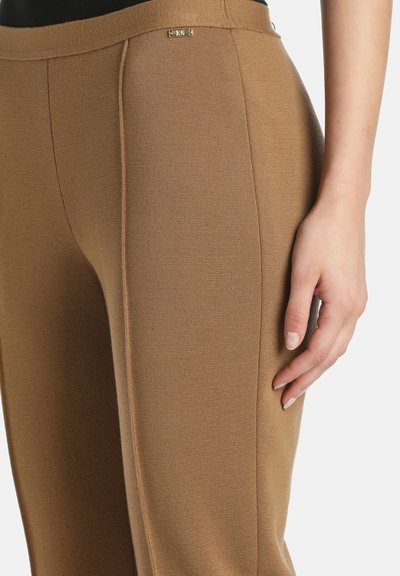 Smeđe pletene hlače s teksturiranim završetkom, slim fit kroja i malim zlatnim logom blizu struka s lijeve strane.