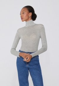 Szary dopasowany sweter z golfem, z długimi rękawami, wykonany z miękkiej dzianiny. W połączeniu z niebieskimi dżinsami o wysokim stanie.