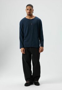 Blauw gebreid shirt met lange mouwen, een losse pasvorm en afgewerkte distressed details, gecombineerd met zwarte broek met wijde pijpen en stevige zwarte schoenen.