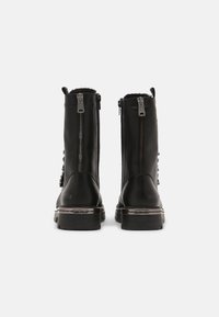 Botines de cuero negro con dos cremalleras laterales, suela robusta y superficie texturizada, con acentos decorativos a lo largo del costado.