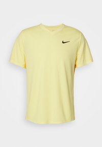 Gul Nike t-shirt med v-hals, korta ärmar och en svart swoosh-logotyp på vänster bröst. Slät textur och avslappnad passform.