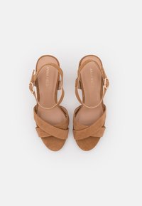 Brown suede sandals with cross-strap design, ankle strap with buckle, rounded toe, and smooth inner sole. Brand name embossed inside.