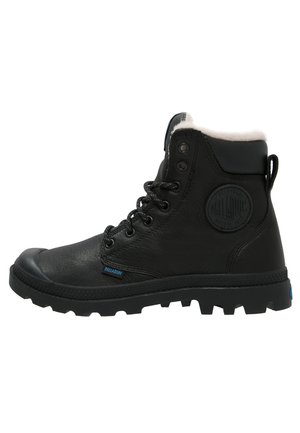 Black leather boot with a faux fur collar, lace-up front, and rubber sole. Features a circular logo patch on the side and textured detailing.