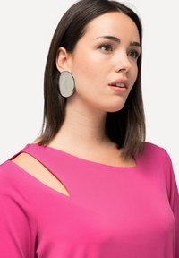 Blusa rosa con un taglio unico sulle spalle, abbinata a grandi orecchini ovali in argento e bianco marmorizzato. Tessuto dalla texture liscia e design moderno.