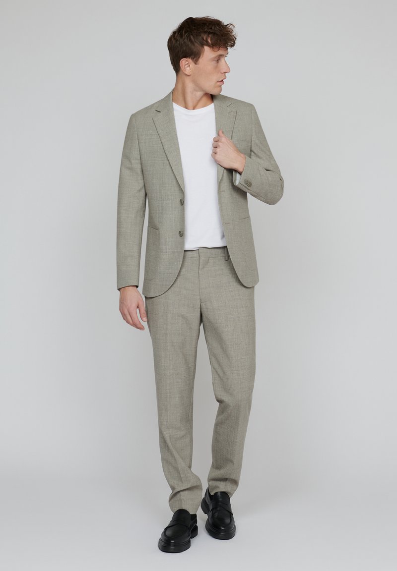 Jasnoszary garnitur dopasowany z wzorem w kratę, zestawiony z białą koszulką i czarnymi butami. Dopasowany krój i wyraźnie zarysowana sylwetka.