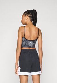 Čierny crop top so vzorom hadieho kožucha s tenkými ramienkami v kombinácii s čiernymi šortkami s bielym lemovaním a bočnými akcentmi. Mäk materiál, športový strih.