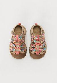 Beige sandaalit, joissa on moniväriset kukkavyöt, säädettävät sulkimet ja ruskea kumipohja. Teksturoitu sisäpohja ja vahvistetut reunat.