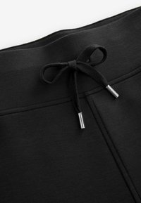 Pantaloni della tuta neri con una superficie testurizzata, dotati di una vita con coulisse e punte in metallo e dettagli di cucitura lungo i lati.