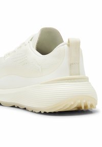 Białe obuwie z teksturowaną, syntetyczną cholewką, wyposażone w pętelkę z tyłu, ozdobione logo oraz posiadające żłobioną, amortyzowaną podeszwę.