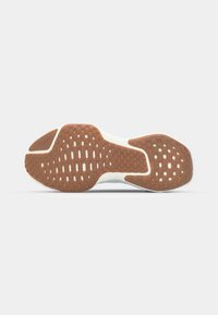 Shoe outsole featuring a brown rubber material with textured grip patterns, outlined by a light-colored midsole and smooth edges.
