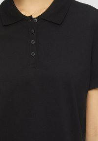Polo noir avec un col, patte de boutonnage à cinq boutons et manches courtes, fabriqué en coton texturé.