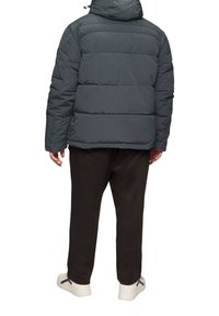 Donsjack in donkergrijs, met een horizontaal gestikt patroon, capuchon en een ritssluiting aan de voorkant. Combinatie met zwarte broeken en witte sneakers.
