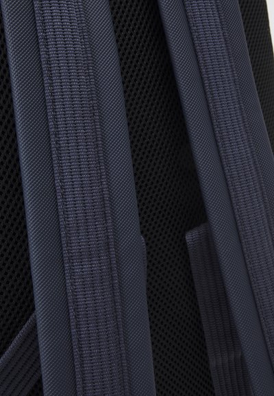 Tissu en maille noire avec des bretelles structurées en bleu foncé présentant un design texturé. Les bretelles sont épaisses et renforcées pour plus de durabilité.