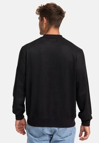Chaqueta bomber negra con una textura suave, puños y dobladillo acanalados. Presenta un cuello simulado y un corte relajado, combinada con unos vaqueros de color azul claro.