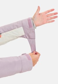 Purple and white jacket cuff with velcro strap and smooth texture. Arm is raised, showing the adjustable fastening detail.