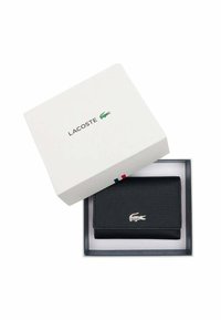 Billetera Lacoste negra en material texturizado dentro de una caja blanca con el logo. Presenta un emblema de cocodrilo plateado y un diseño minimalista.
