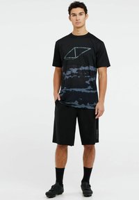 Mustat urheilupaidat, joissa on sininen kamppailukuosi, kosteusnielu materiaali, lyhyet hihat ja logo edessä; yhdistettynä mustiin shortseihin.