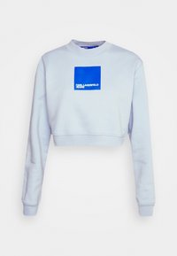 Jasnoniebieski krótki sweatshirt z okrągłym dekoltem, z kwadratową grafiką w niebiesko-białych kolorach z napisem "KARL LAGERFELD JEANS." Miękka tekstura.