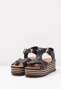 Black leather sandals with cross straps and adjustable buckle. Features a stacked platform with alternating black and tan stripes.