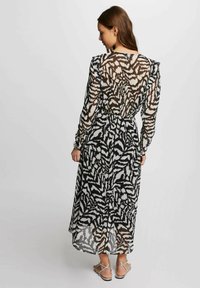 Abito lungo e trasparente con un motivo astratto in bianco e nero, caratterizzato da maniche lunghe, vita strizzata e un orlo fluido che arriva fino alle caviglie.