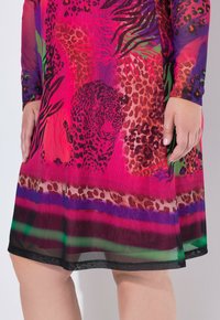 Vestido rosa brillante con mangas largas que presenta un estampado de jaguar y leopardo, con patrones de hojas verdes y moradas, llevado por una persona con las manos visibles.