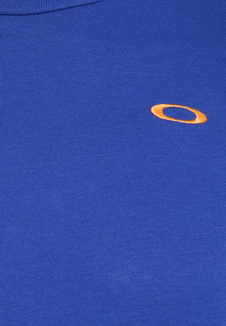 T-shirt en coton bleu avec un col rond, arborant un petit logo circulaire orange sur la poitrine gauche et une texture lisse.