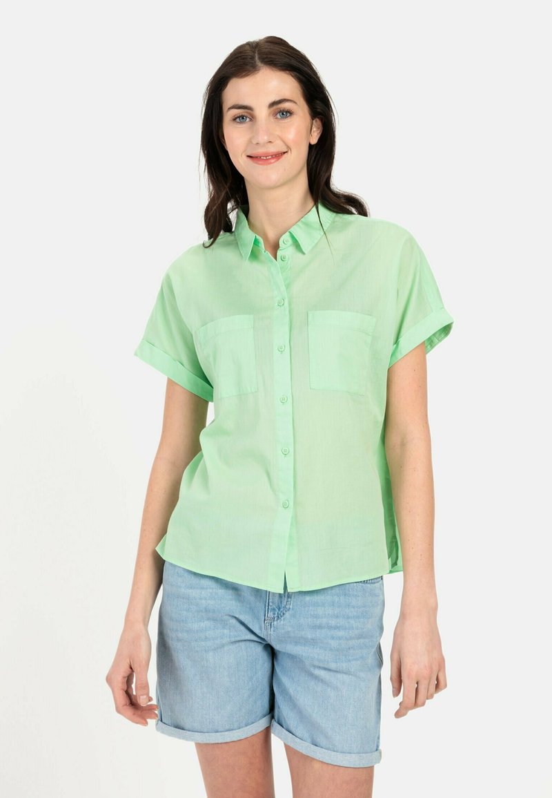 Korte mouwen, knoopsluiting shirt in lichtgroen, met twee borstzakken en een relaxte pasvorm, gecombineerd met opgerolde jeansshorts.