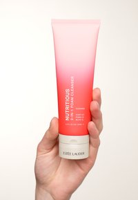 Rosa ombre-tub av Estee Lauder Nutritious 2-i-1 skumrengöring, med vit text och en cirkulär bas. Innehåller 4,2 fl oz (125 mL).