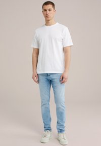 Balts kokvilnas T-krekls ar īsām piedurknēm, apvienots ar gaiši ziliem džinsiem un baltiem sneakeriem. Vienkāršs, klasiskā dizaina, minimālas detaļas.