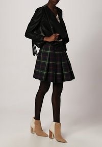 Chaqueta de cuero negra envolvente, falda acampanada de cuadros verdes y marinos, medias negras, botas de tobillo beige con una franja en contraste y tacón en bloque.