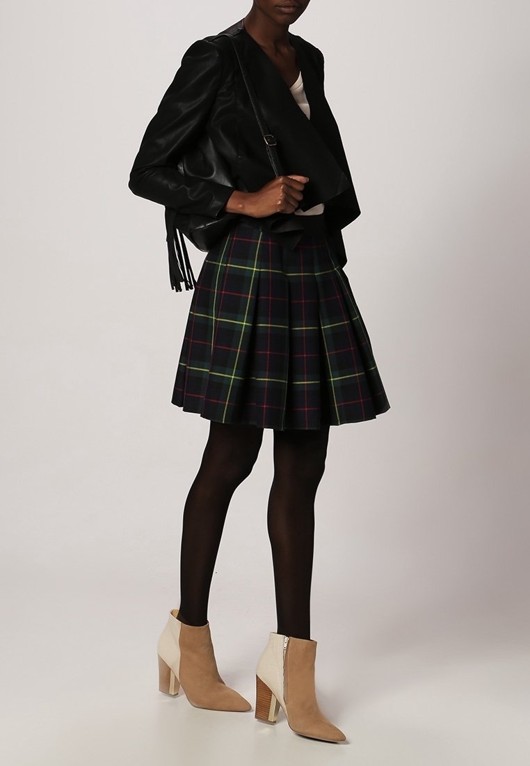 Chaqueta de cuero negra envolvente, falda acampanada de cuadros verdes y marinos, medias negras, botas de tobillo beige con una franja en contraste y tacón en bloque.