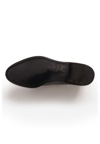 Suola di scarpa in pelle nera con un profilo elegante, texture liscia, bordo arrotondato e piccole perforazioni circolari vicino al tallone.